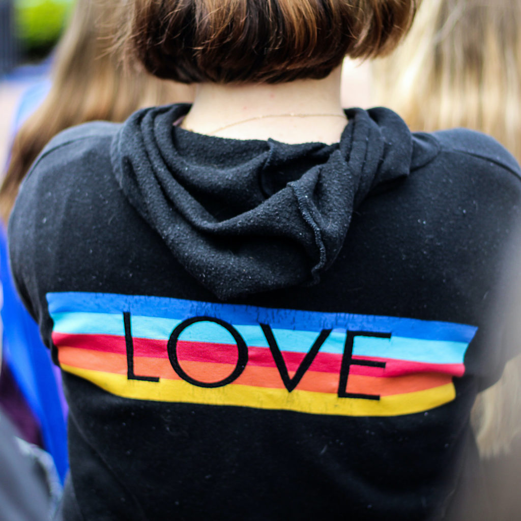 Photo of a young person with a sweatshirt that reads LOVE with a rainbow behind it. 
